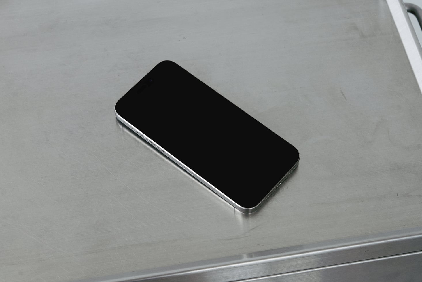Smartphone with black screen sitting on brushed metal surface at slight angle
