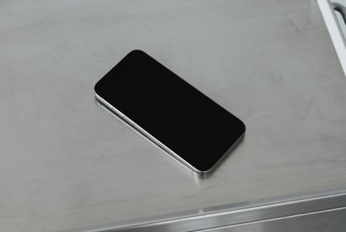 Smartphone with black screen sitting on brushed metal surface at slight angle