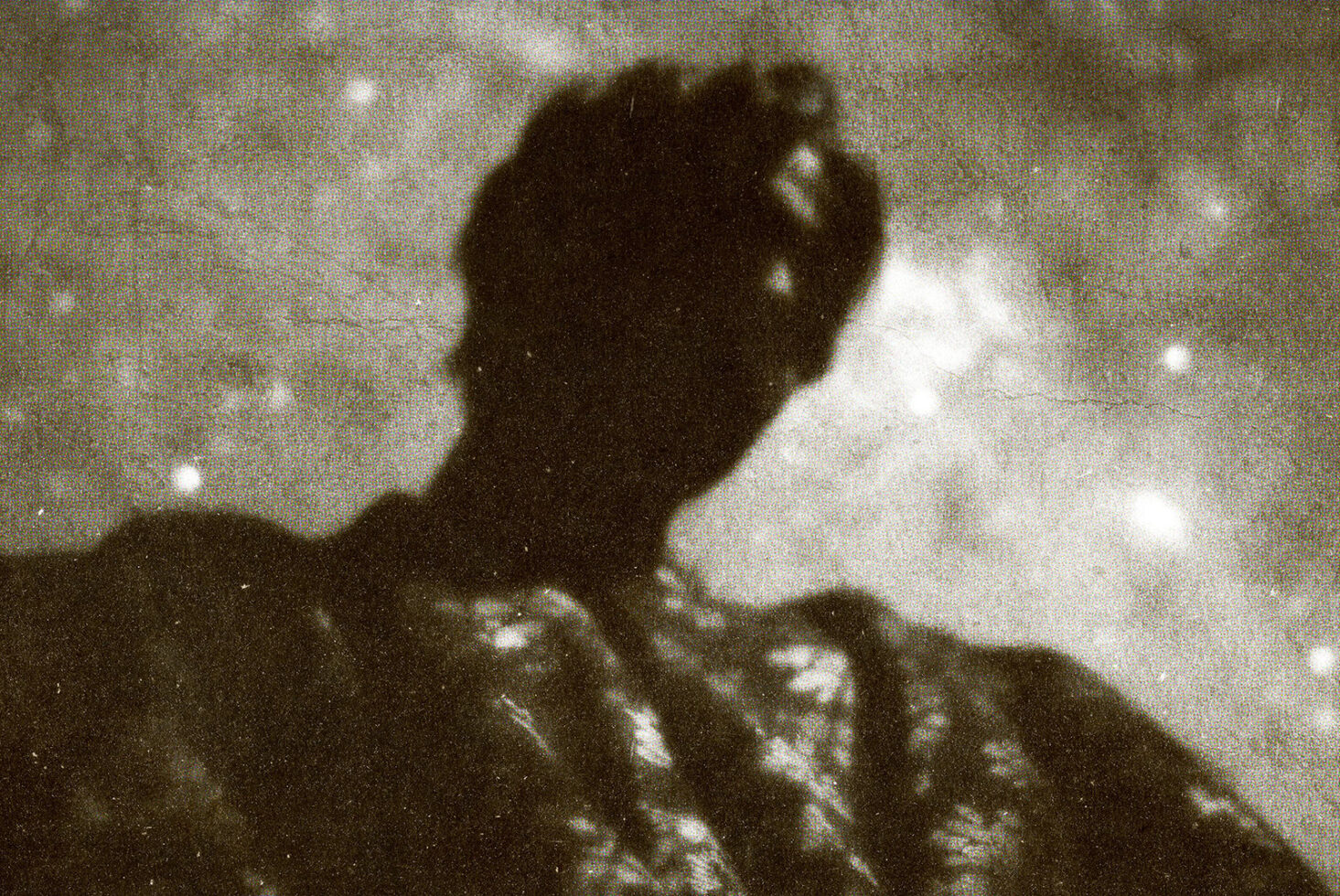 Grainy vintage photo of silhouetted figure against cloudy sky with film grain texture