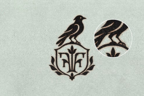 Vintage bird crest logo with ornamental shield on textured paper, close-up detail shown