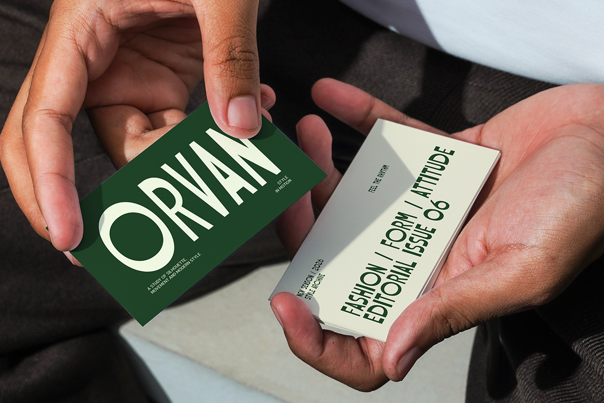 Two hands holding business cards, green card says "ORVAHN" in white, cream card shows editorial masthead text