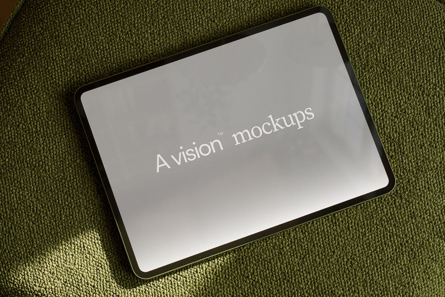 Tablet with rounded black frame lying on olive green textured fabric showing blank screen mockup