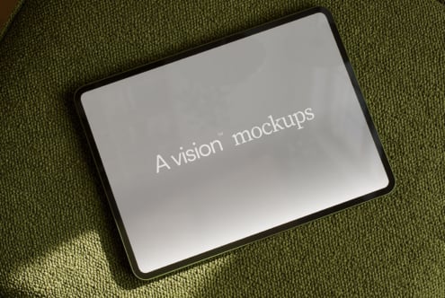 Tablet with rounded black frame lying on olive green textured fabric showing blank screen mockup