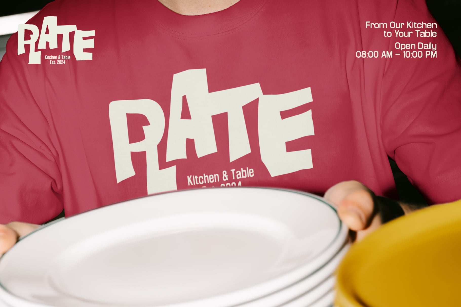 Person wearing maroon PATE Kitchen & Table tee holding empty plate mockup