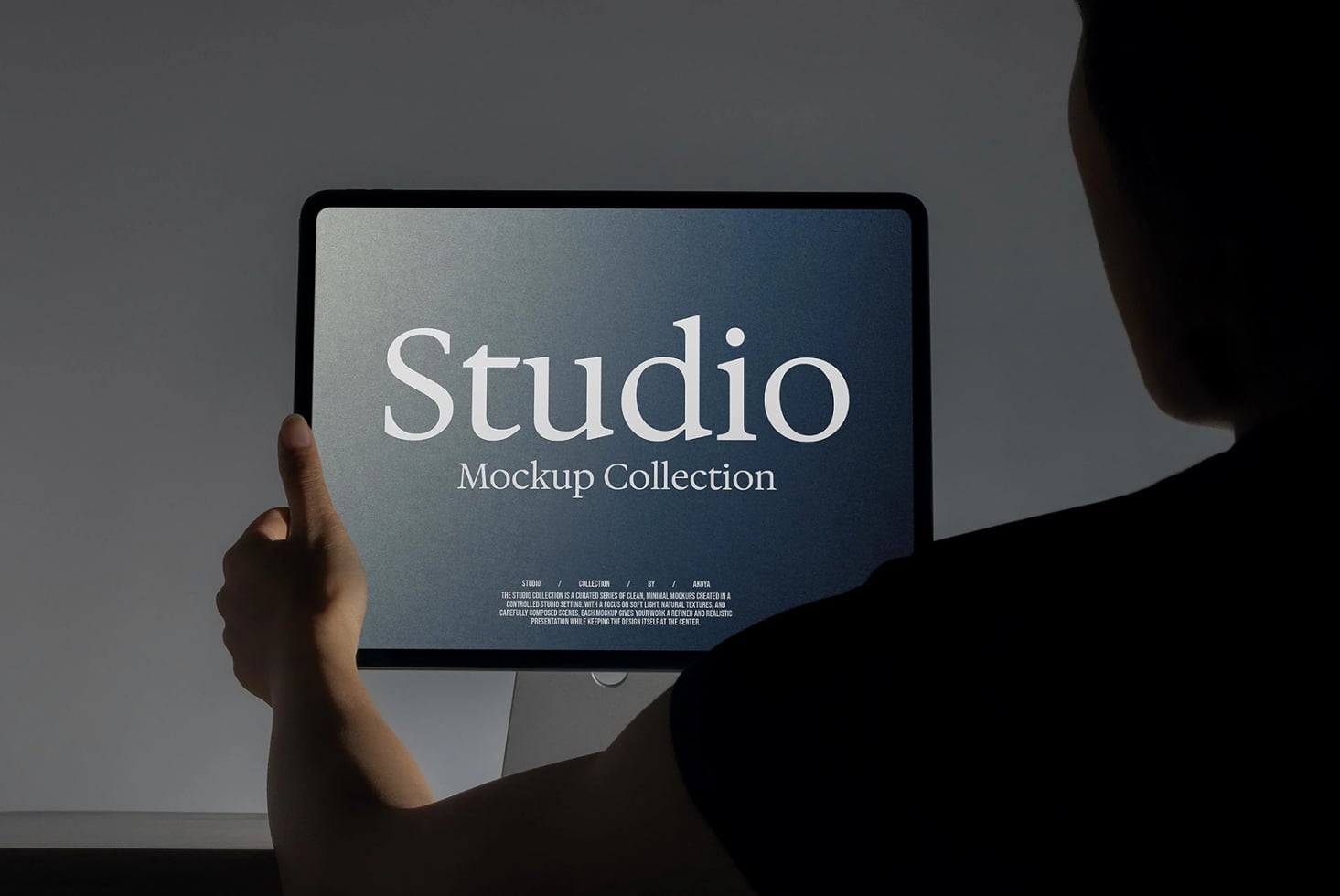 Hand holding tablet displaying Studio Mockup Collection with gradient blue screen