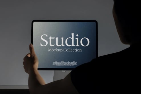 Hand holding tablet displaying Studio Mockup Collection with gradient blue screen