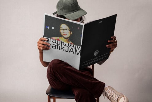 Person sitting on chair reading open magazine mockup with portrait artwork visible on cover