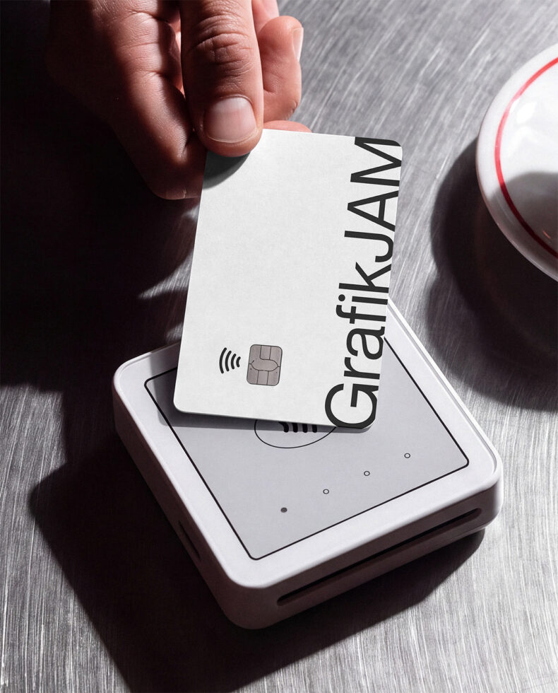 Hand holding contactless credit card over white payment terminal on brushed metal surface