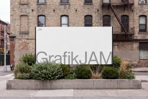 Large white billboard mockup on urban street with brick buildings, concrete planter box with greenery below