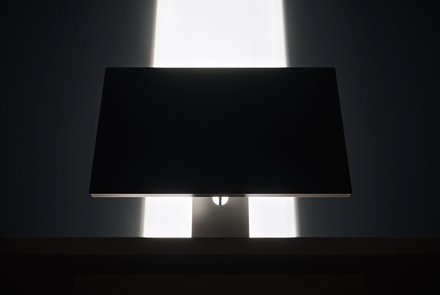 Monitor mockup with black screen on stand, backlit by bright window