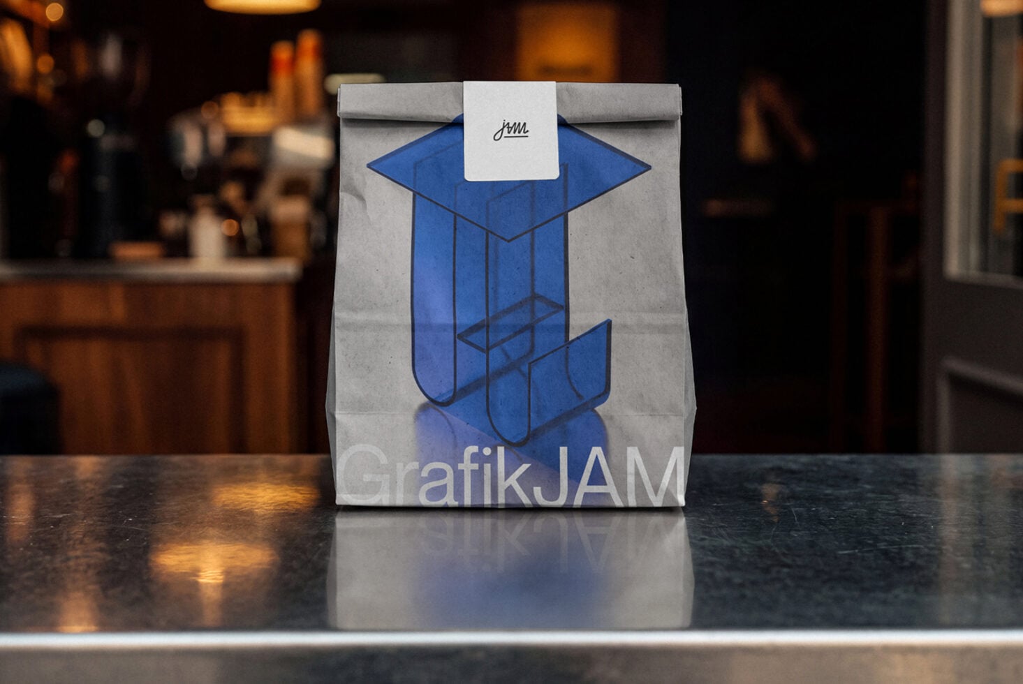 Gray paper bag with blue geometric shapes, white label with handwritten logo on dark counter