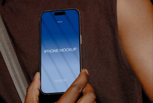 Hand holding iPhone with blue gradient screen displaying mockup text on fabric background
