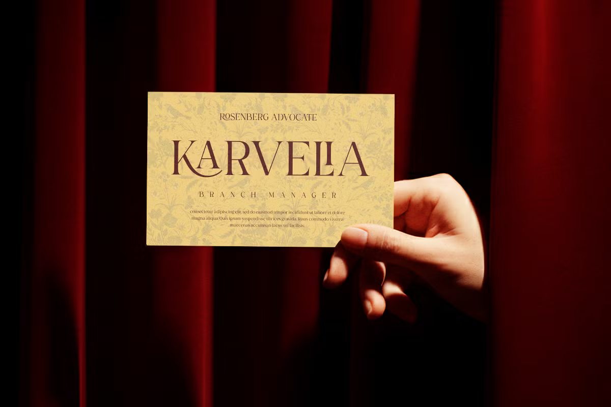 Hand holding gold business card with "Karveela" serif typography on red striped backdrop