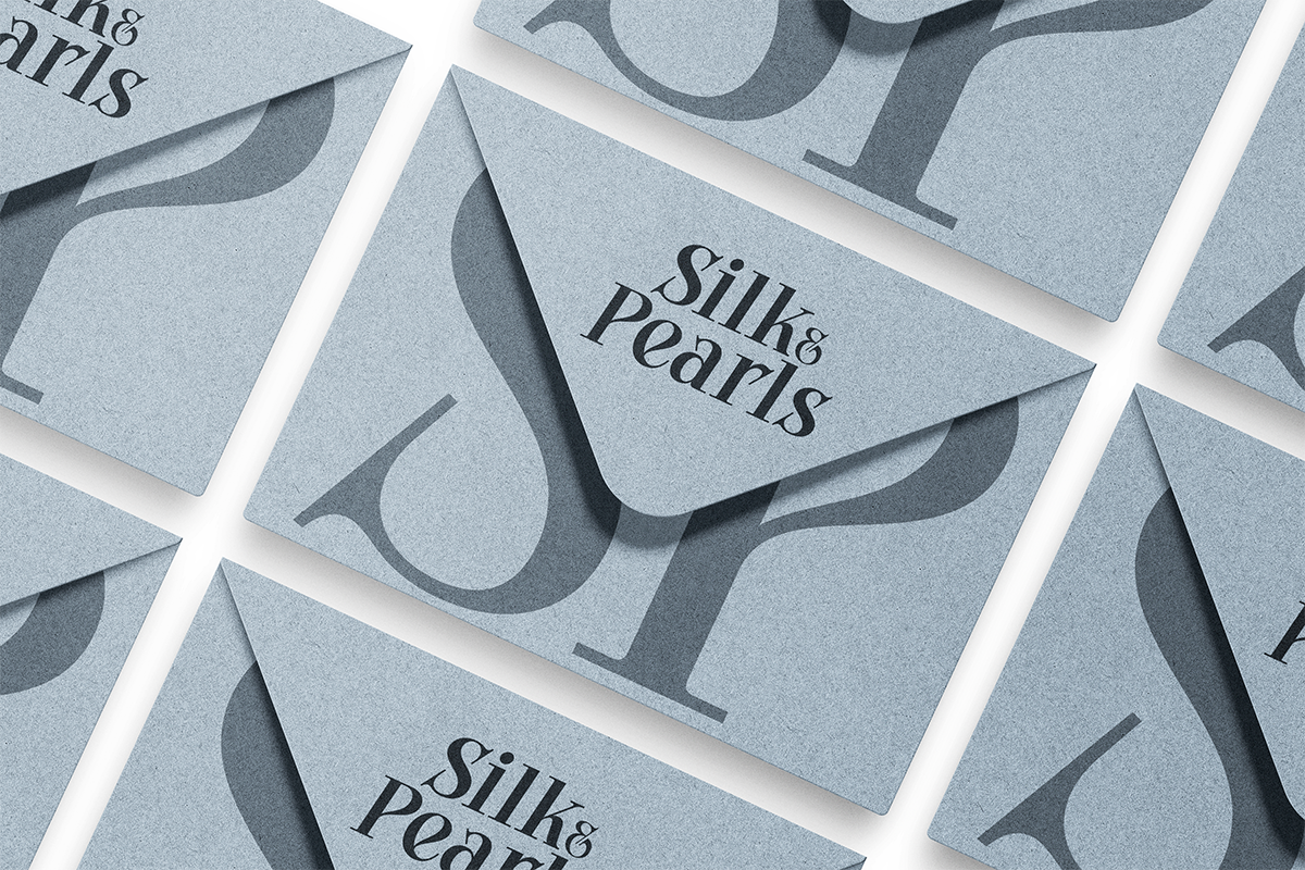 Silk Pearls business cards in dusty blue with layered abstract shapes, overhead flat lay