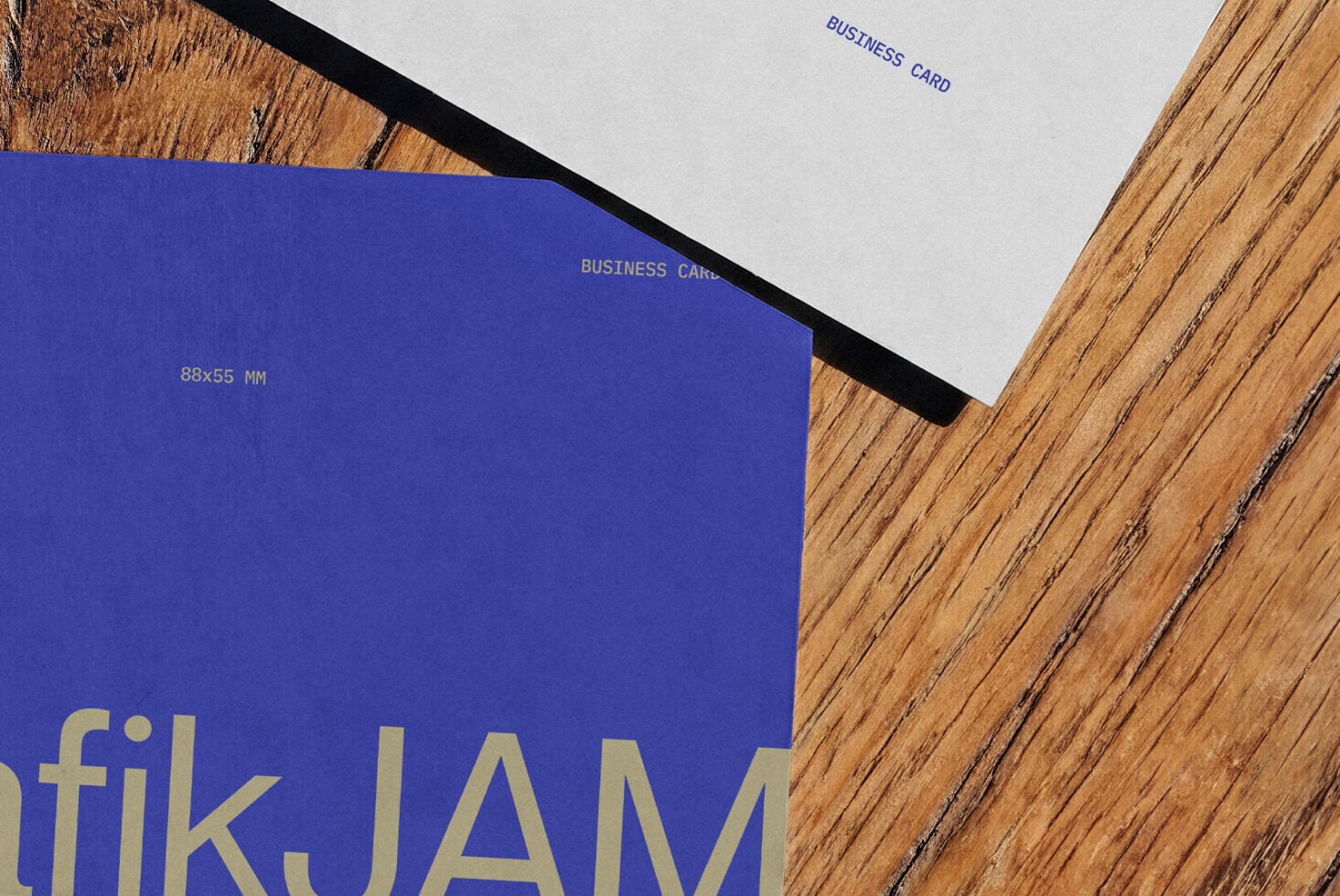 Bright blue business card mockup with gold foil text sitting on warm wood surface next to white card