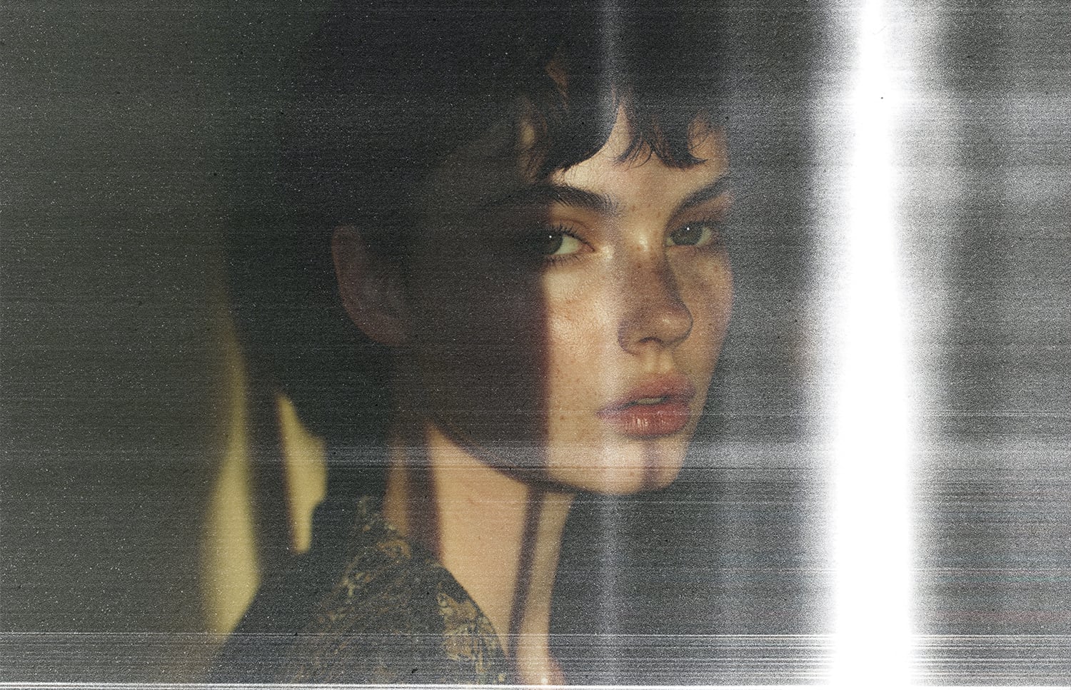 Moody portrait of person with short dark hair, grainy film texture, soft light streaks cutting through frame