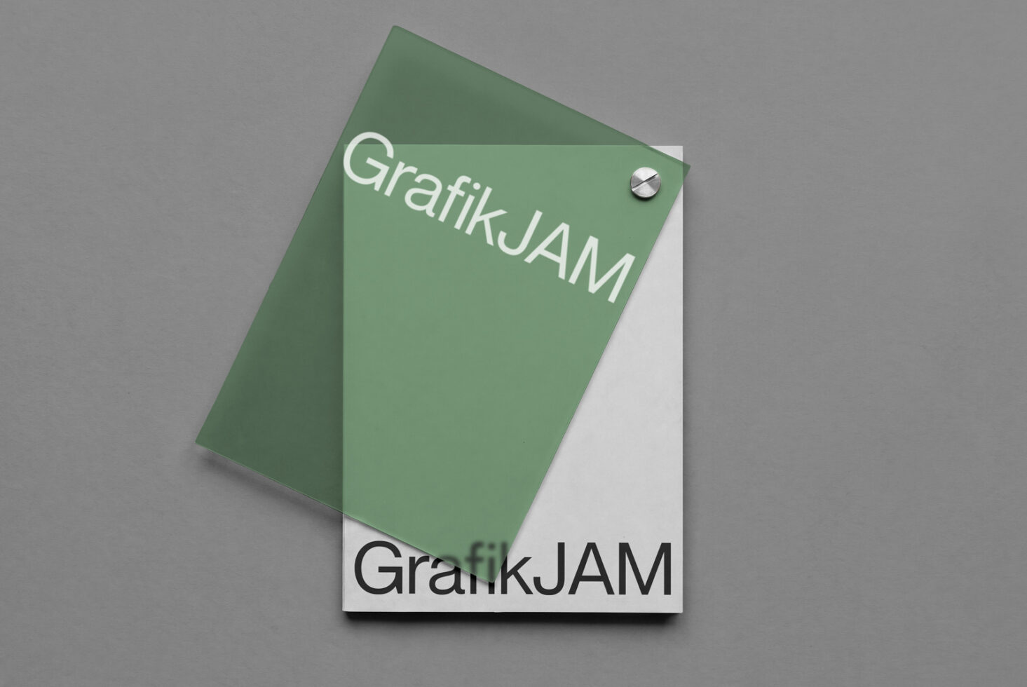 Tilted green notebook mockup with GrafikJAM branding on sage background with metal screw detail