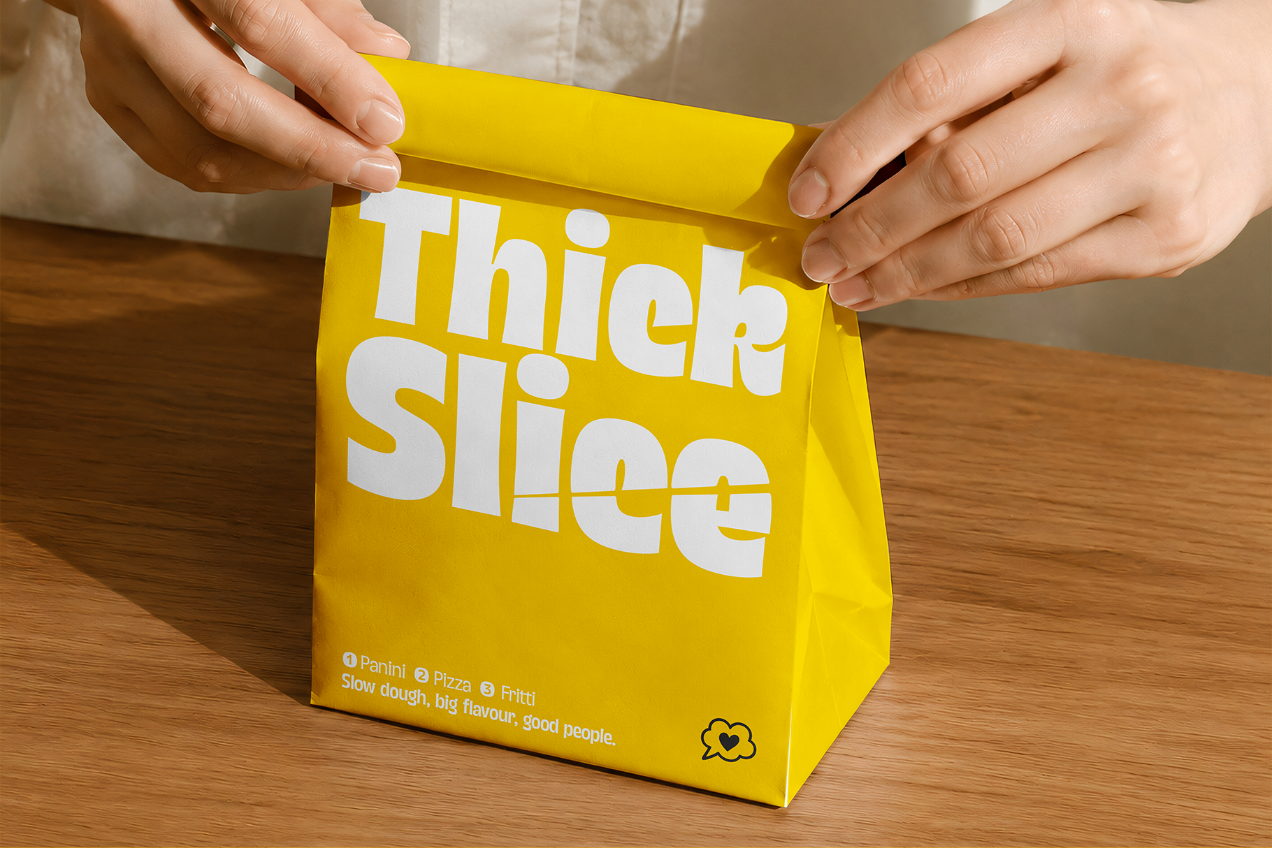 Hands holding bright yellow food bag with "Thick Slice" branding in white lettering on wooden table