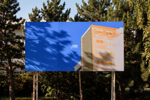 Outdoor billboard mockup with split blue sky plus orange brick building photo, surrounded by pine trees