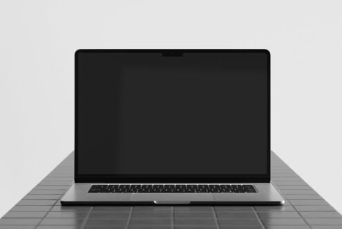 Laptop mockup with black screen sitting on gray tiled surface, front perspective view