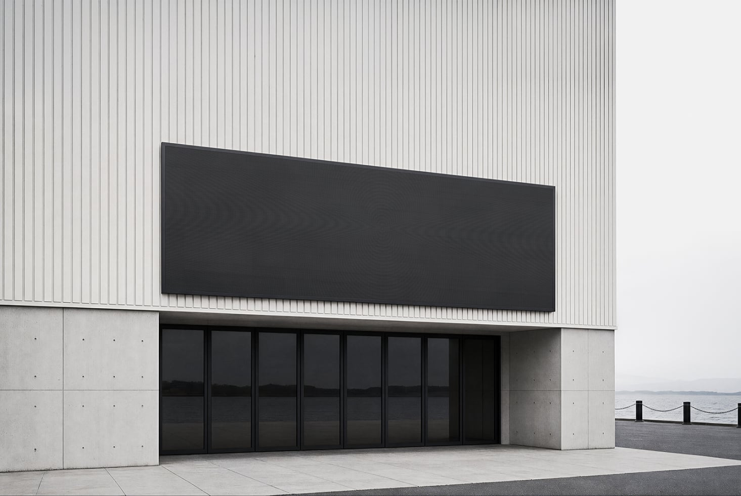 Minimalist storefront with black signage on corrugated metal, concrete facade, oceanside setting