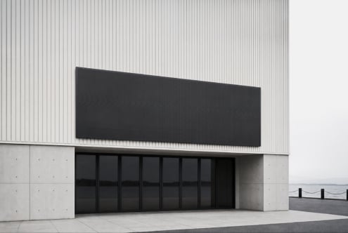 Minimalist storefront with black signage on corrugated metal, concrete facade, oceanside setting