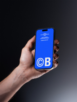 Hand holding iPhone with bright blue screen displaying CB logo with text overlay