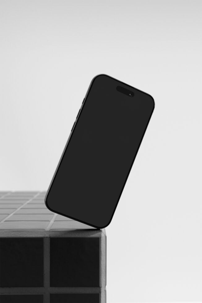 Black iPhone leaning on concrete block, angled shot on minimal gray background