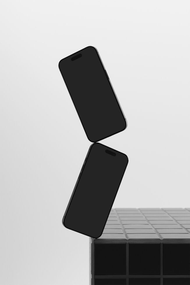 Two black iPhones stacked at angles on geometric blocks, minimal studio setup