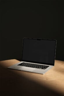 Silver MacBook Pro sitting on wood table with dark background, screen off