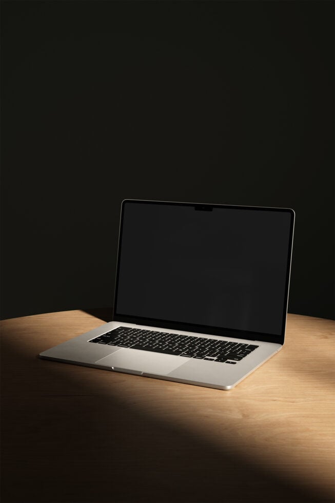 Silver MacBook Pro sitting on wood table with dark background, screen off