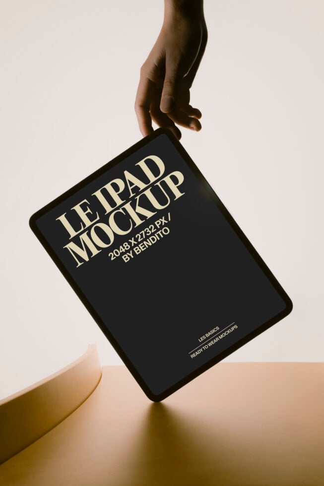 Hand holding black iPad mockup with cream typography on neutral background