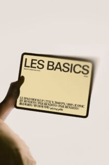 Hand holding iPad mockup with Les Basics cream screen, multilingual text visible