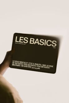 Hand holding black iPad mockup showing Les Basics design with multilingual text