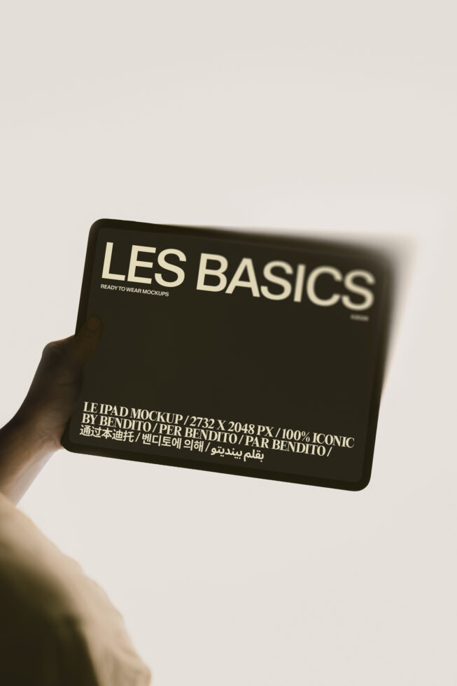 Hand holding black iPad mockup showing Les Basics design with multilingual text
