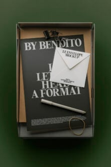 Flat lay mockup of black poster, white envelope, pen, gold ring, binder clip in cardboard box