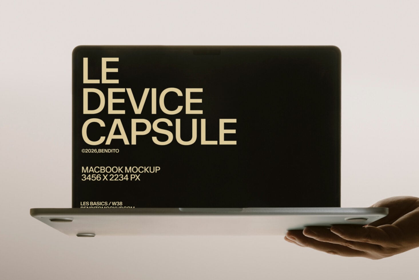Hands holding open MacBook with cream text on black screen showing Le Device Capsule mockup