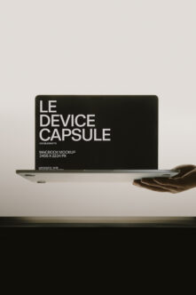 Hand holding MacBook with black screen showing "Le Device Capsule" text mockup