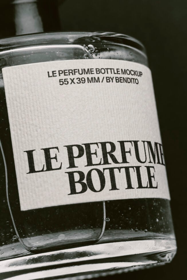 Clear glass perfume bottle with white label showing bold serif typography on dark background