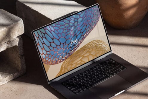 Laptop mockup displaying vibrant organic mesh pattern artwork on screen in sunlit concrete setting