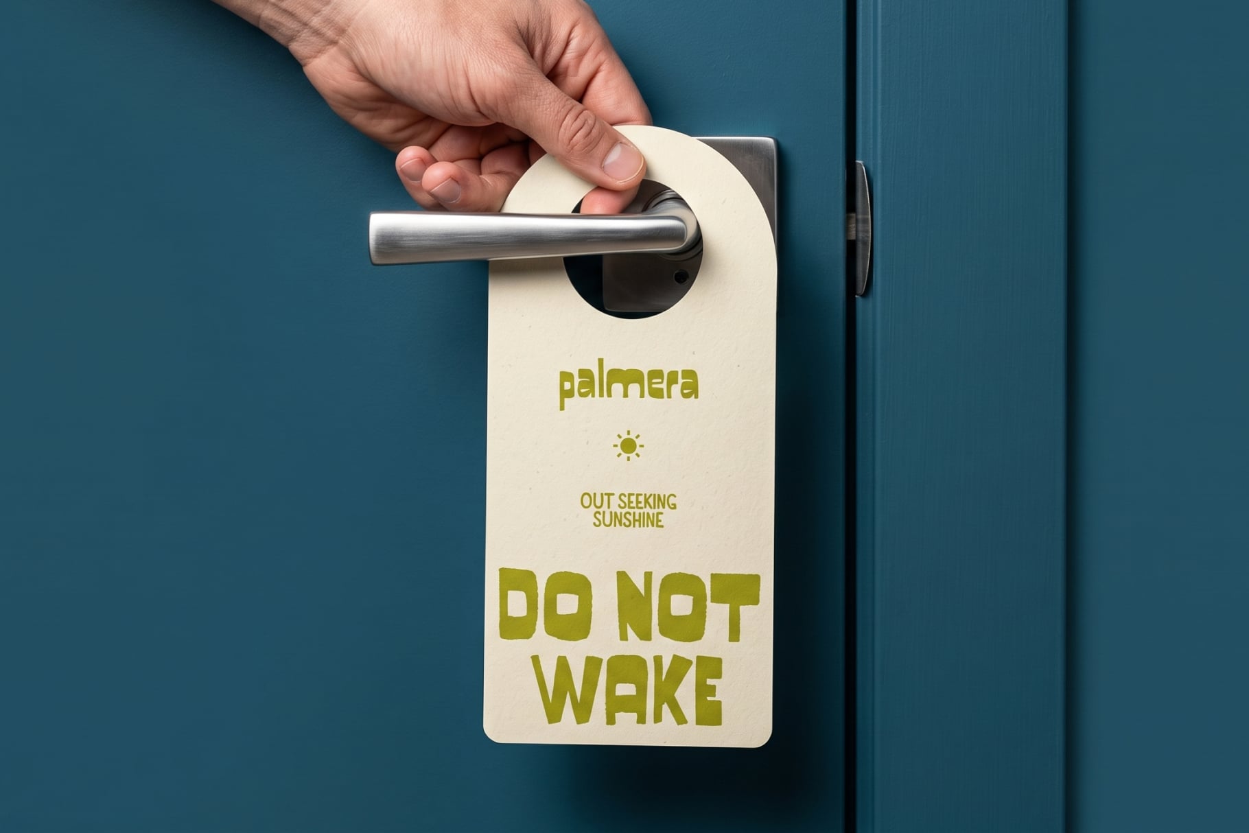 Hand hanging cream door hanger on teal wall showing Palmera brand with do not wake messaging