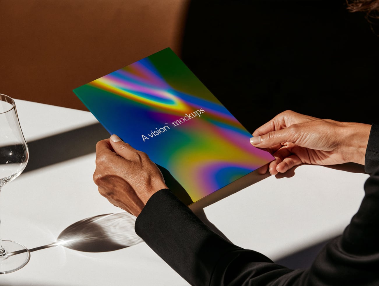 Hands holding colorful gradient book mockup with "A vision mockups" text on white table