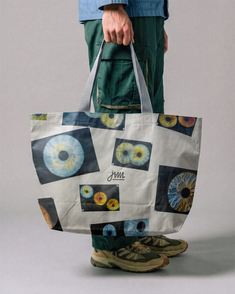 Person holding cream tote bag with colorful iris eye prints scattered across front