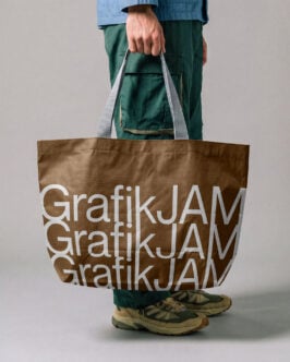 Person holding brown tote bag with repeated white text mockup, casual styling