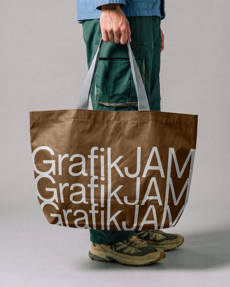 Person holding brown tote bag with repeated white text mockup, casual styling