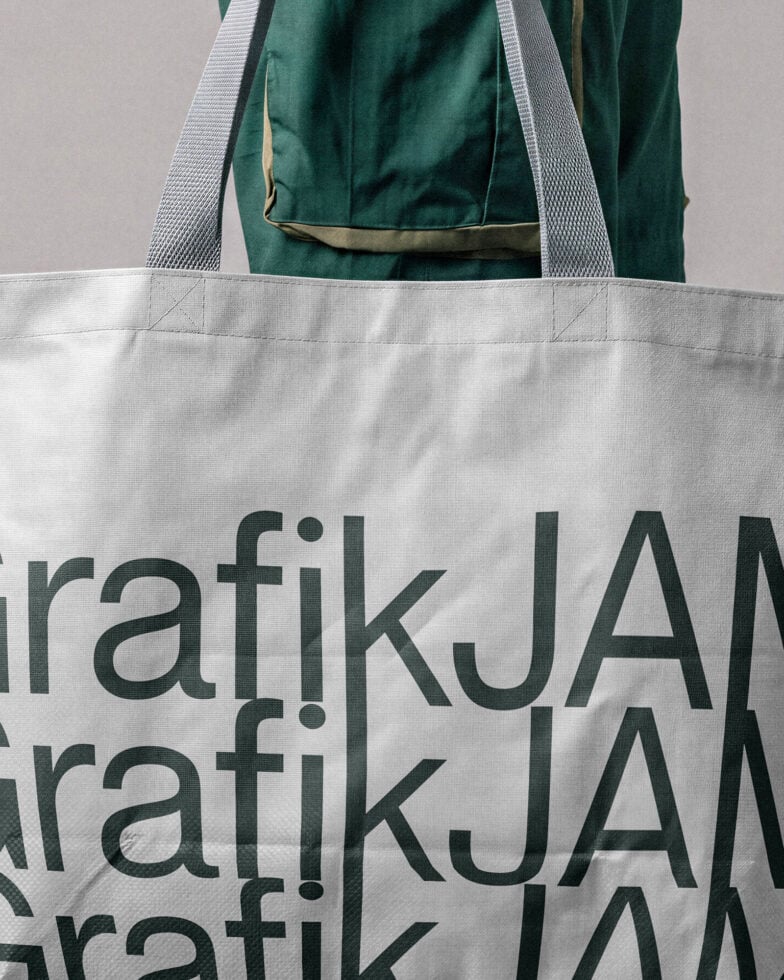 Canvas tote bag mockup with dark green jacket, bold serif typography in forest green