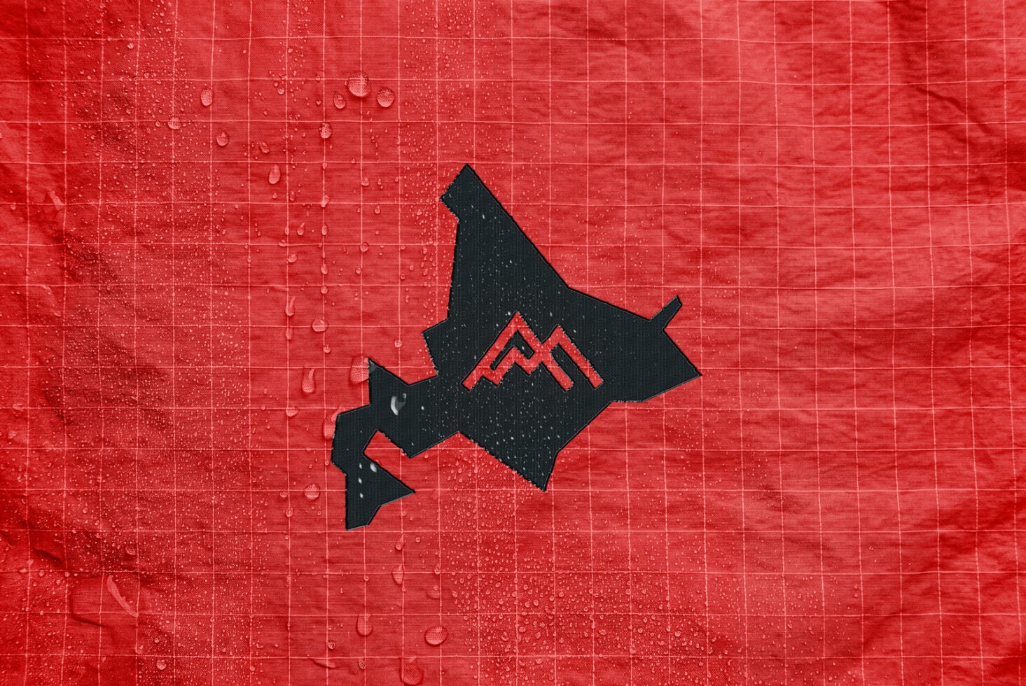 Black mountain logo with red peaks on wet red tile background with water droplets
