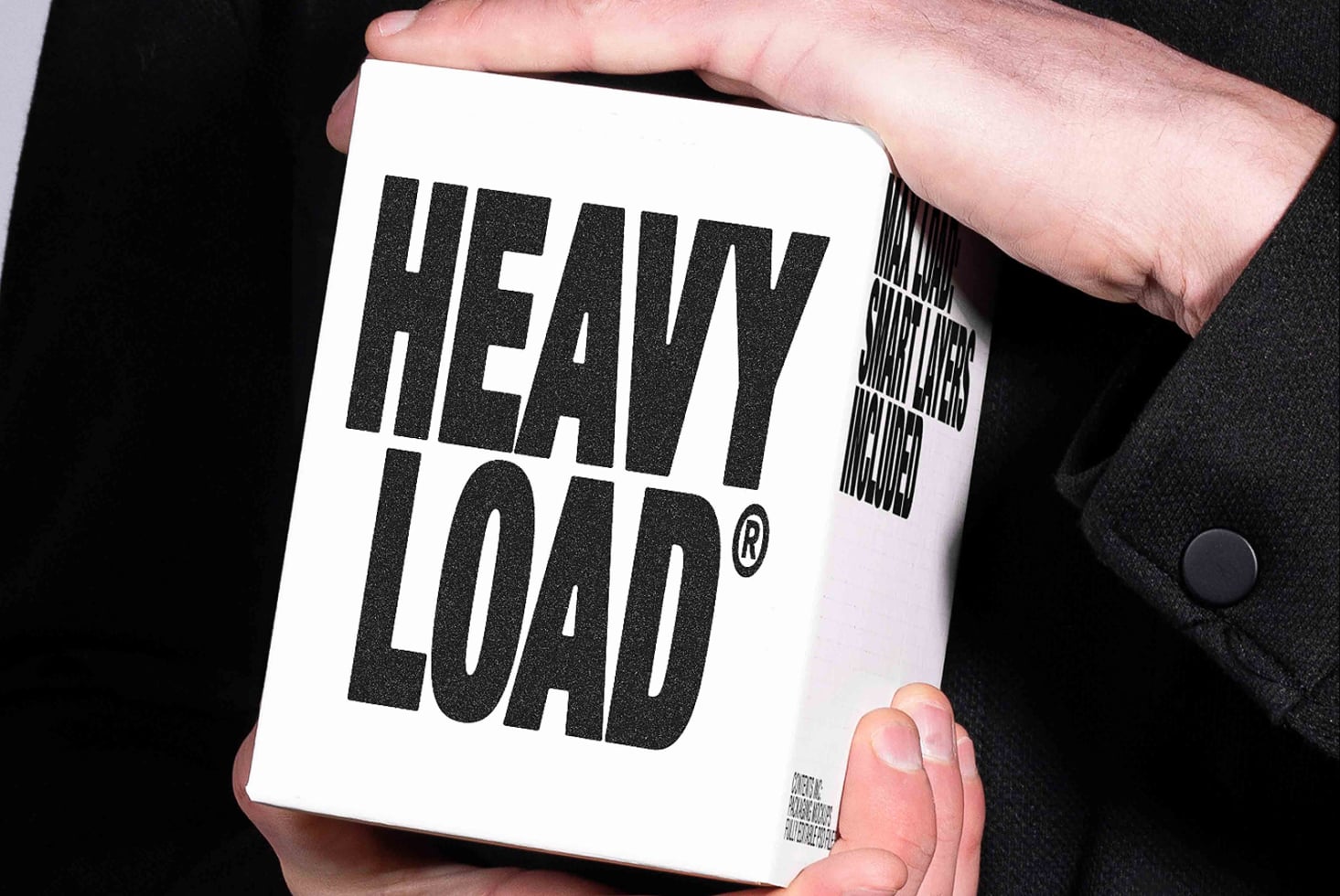 Hand holding white box with bold black "HEAVY LOAD" text plus barcode mockup on dark background