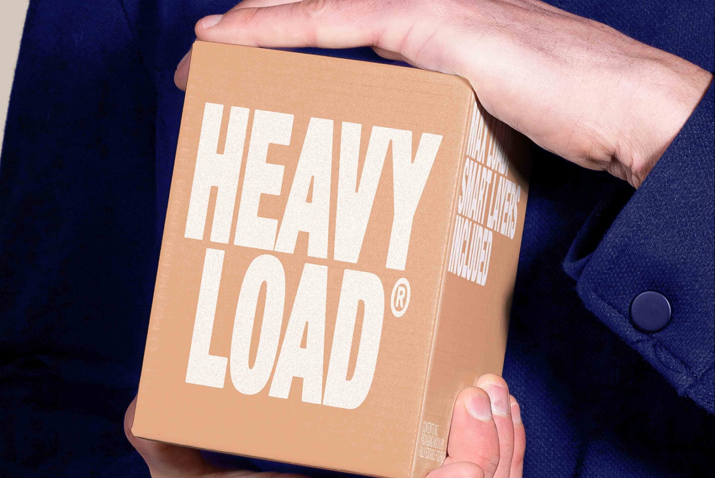 Hands holding kraft box with bold white HEAVY LOAD text plus barcode sticker