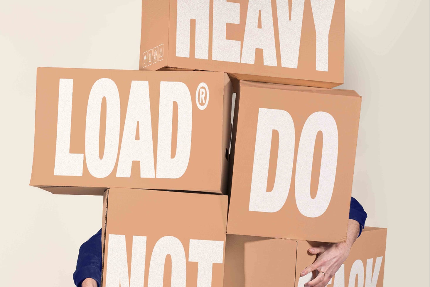 Person stacked under cardboard boxes with oversize bold typography saying heavy load not